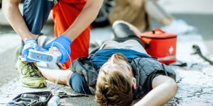 Ambulance worker applying emergency care with defibrillator to the injured bleeding man. Concept of Types of Workers' Compensation Benefits