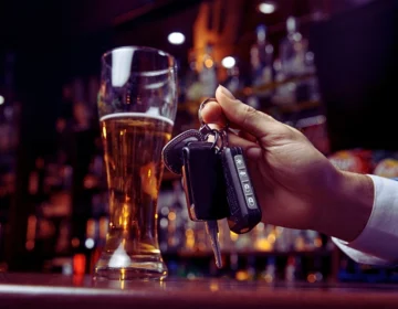 a hand holding car keys next to a glass of beer on a bar counter.