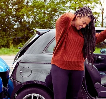 a woman standing outside a small black car, holding her neck as if in pain. Minor Car Crashes