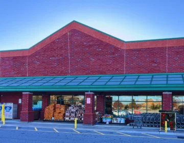 The building has a green awning over the entrance, and there are shopping carts and some stacked items visible near the entrance, indicating it is likely a grocery store or supermarket.
