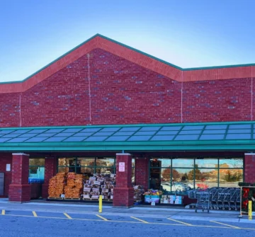 The building has a green awning over the entrance, and there are shopping carts and some stacked items visible near the entrance, indicating it is likely a grocery store or supermarket.