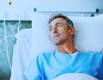 A person lying in a hospital bed wearing a light blue hospital gown. Long-Term Medical Care After a Severe Injury