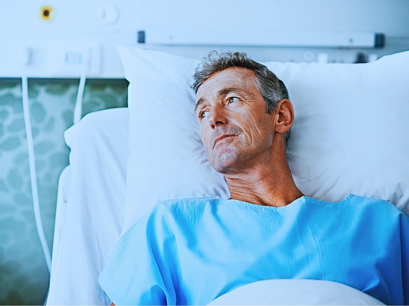 A person lying in a hospital bed wearing a light blue hospital gown. Long-Term Medical Care After a Severe Injury
