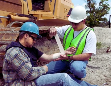 One construction worker providing first aid to an injured coworker at an outdoor job site. When Does a Work Injury Lead to a Lawsuit Instead of Workers’ Compensation