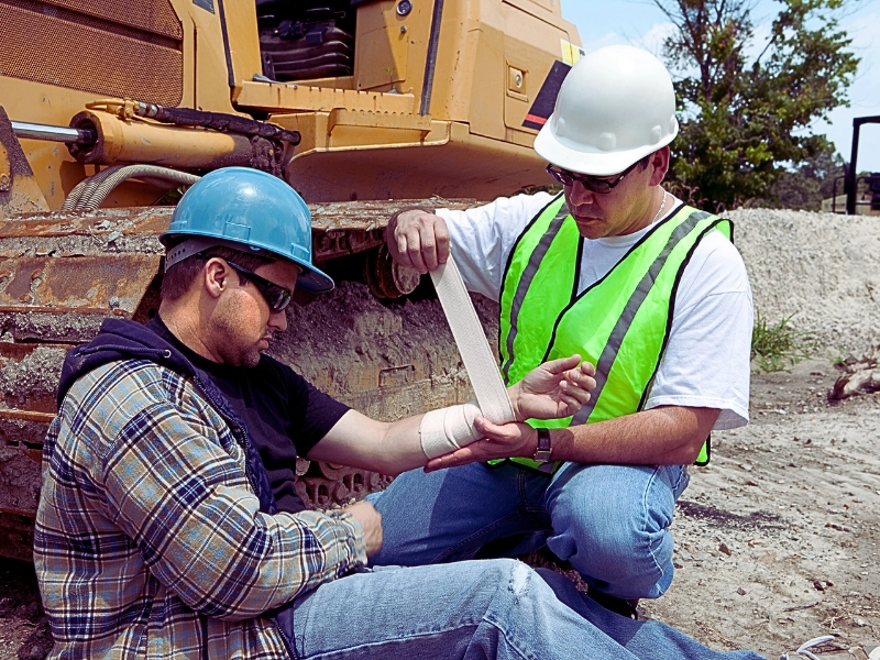 One construction worker providing first aid to an injured coworker at an outdoor job site. When Does a Work Injury Lead to a Lawsuit Instead of Workers’ Compensation