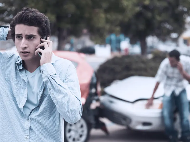 Two boys have been in a car accident and are both on cell phone calls. One of the boys looks noticeably worried. other driver lies about the accident