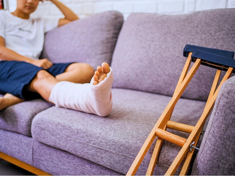 Person resting on couch with cast on leg and crutches. sue after an injury at an apartment complex