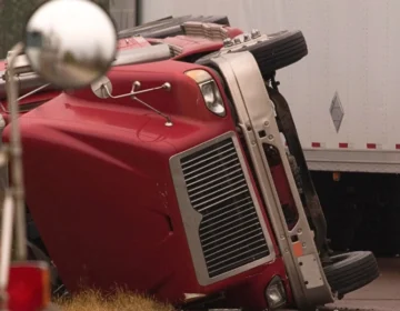 A red semi truck lays on it's side after the commercial truck has brake failure.