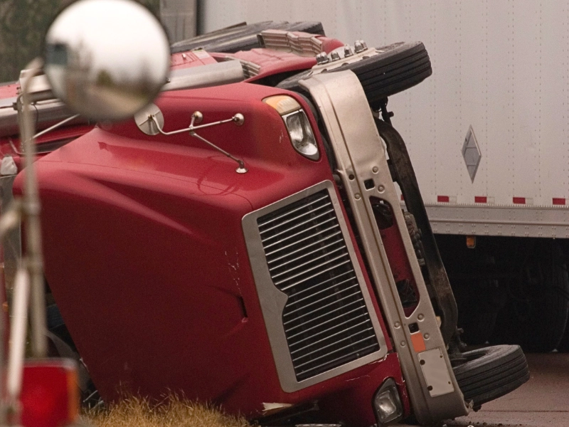 A red semi truck lays on it's side after the commercial truck has brake failure.